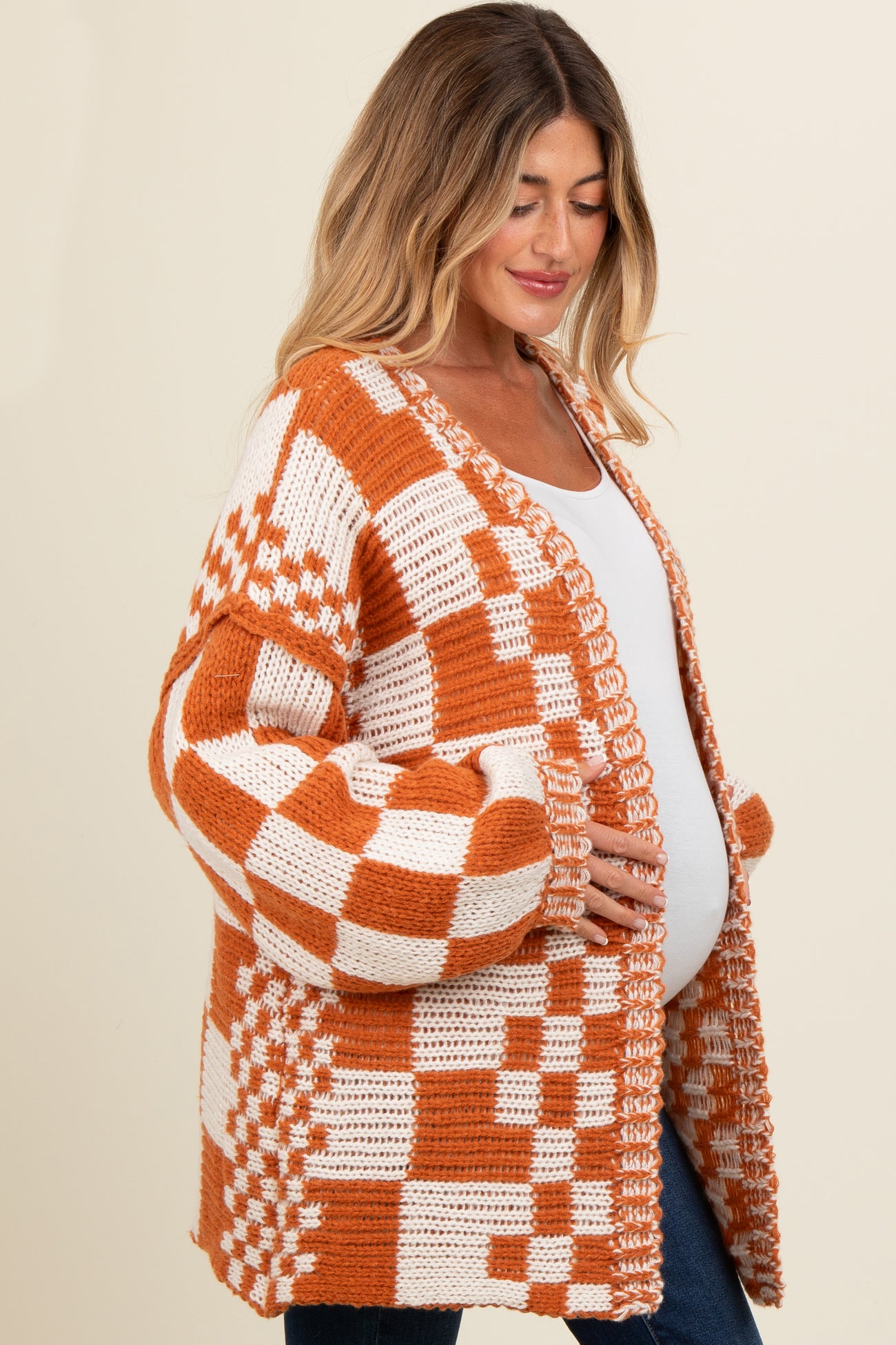 woman wearing a rust and cream checkered maternity cardigan and cradling her baby bump