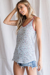 woman wearing a light blue floral tank top with a burgundy trim and distressed denim shorts
