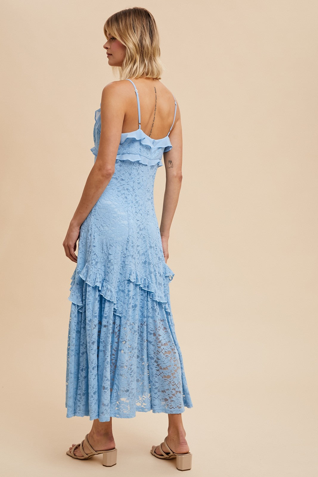 woman wearing a light blue lace maxi dress with ruffled straps and tiers, standing with her back to the camera