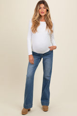 woman wearing a white long sleeve maternity top and blue flared jeans, showing her baby bump