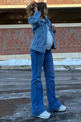 woman wearing a light blue denim jacket and flared jeans showcasing her baby bump in a winter setting