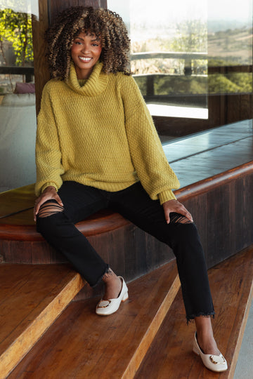 woman wearing a yellow oversized cowl neck maternity sweater with balloon sleeves and black ripped maternity jeans
