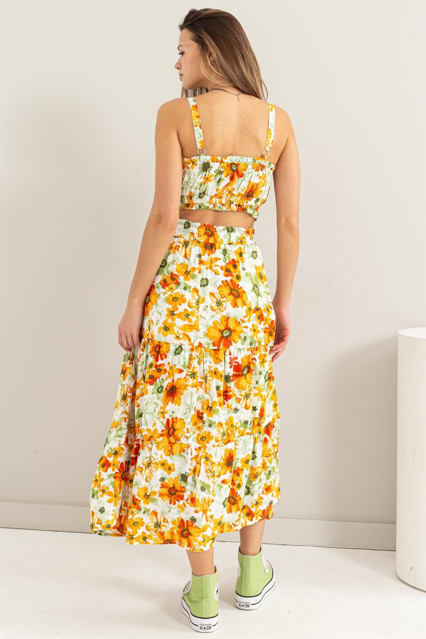 woman wearing a floral two-piece crop top and maxi skirt with bright yellow and orange flowers, paired with green sneakers