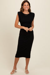woman wearing a black midi dress with shoulder padding and a fitted silhouette, standing and smiling