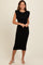 woman wearing a black midi dress with shoulder padding and a fitted silhouette, standing and smiling