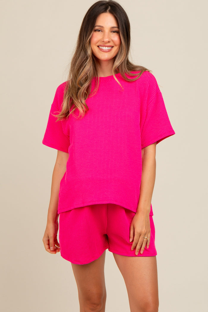 woman wearing a bright pink ribbed short sleeve maternity top and matching shorts, smiling at the camera