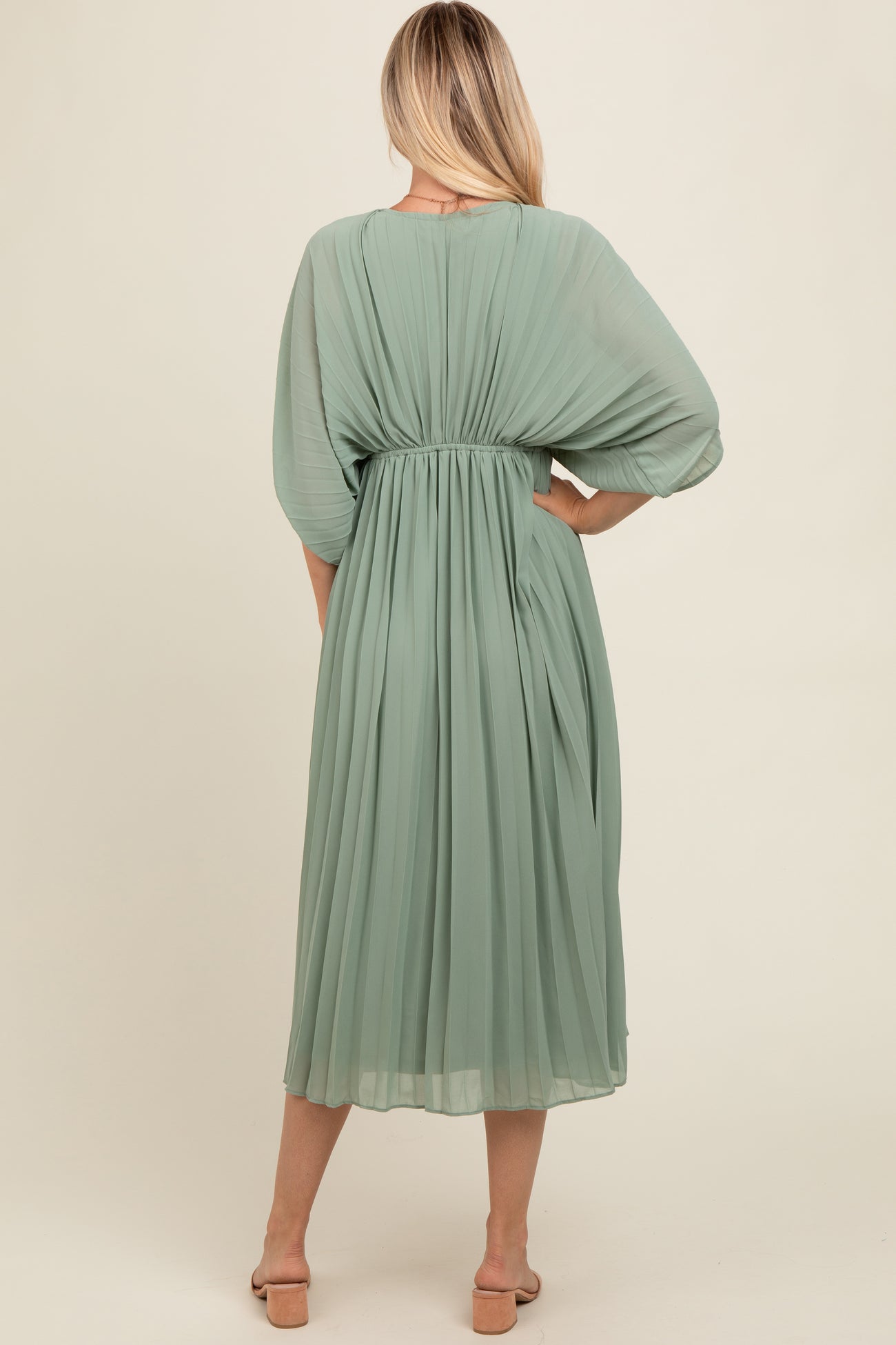 woman wearing a green pleated midi dress with a cinched waist and flowy sleeves, viewed from the back