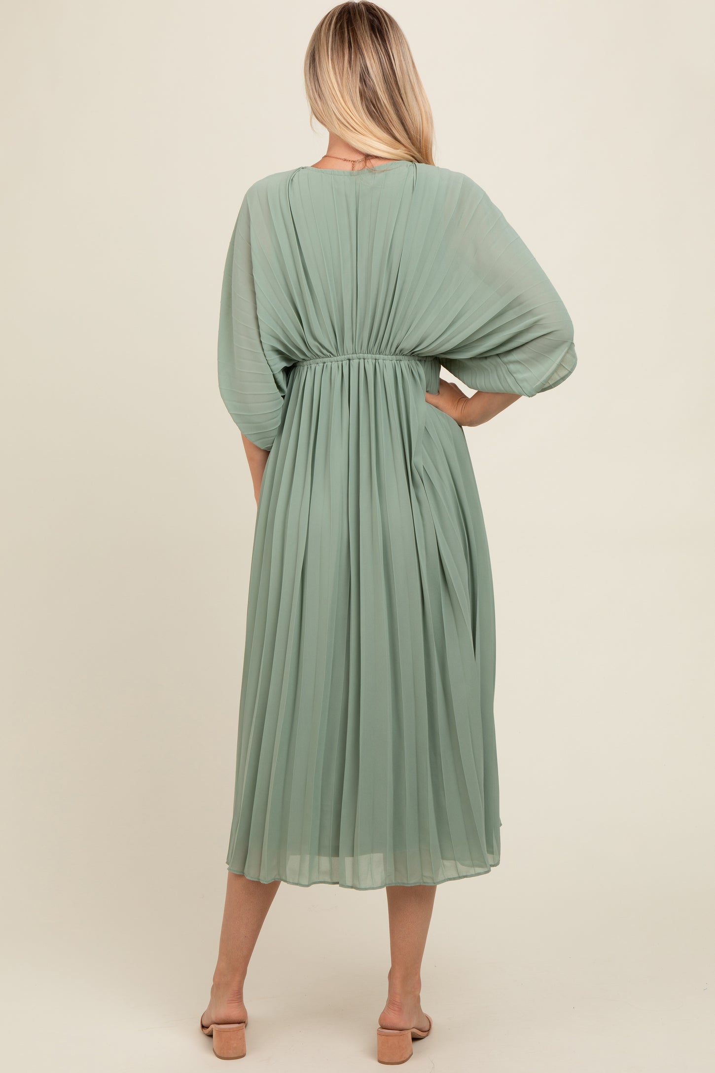woman wearing a green pleated midi dress with a cinched waist and flowy sleeves, viewed from the back