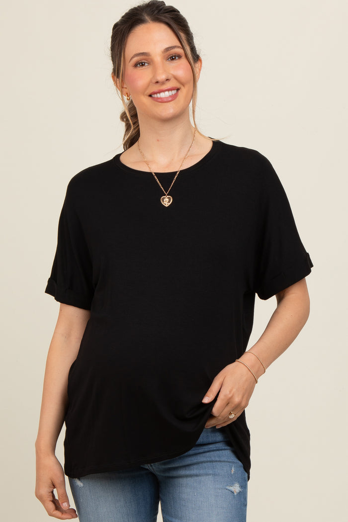woman wearing a black short sleeve maternity top and smiling while showing her baby bump