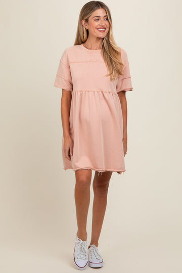 woman wearing a blush pink short sleeve maternity dress with a relaxed fit and distressed hem