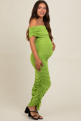 woman wearing a lime green off-the-shoulder maternity dress with side ruching and holding her baby bump