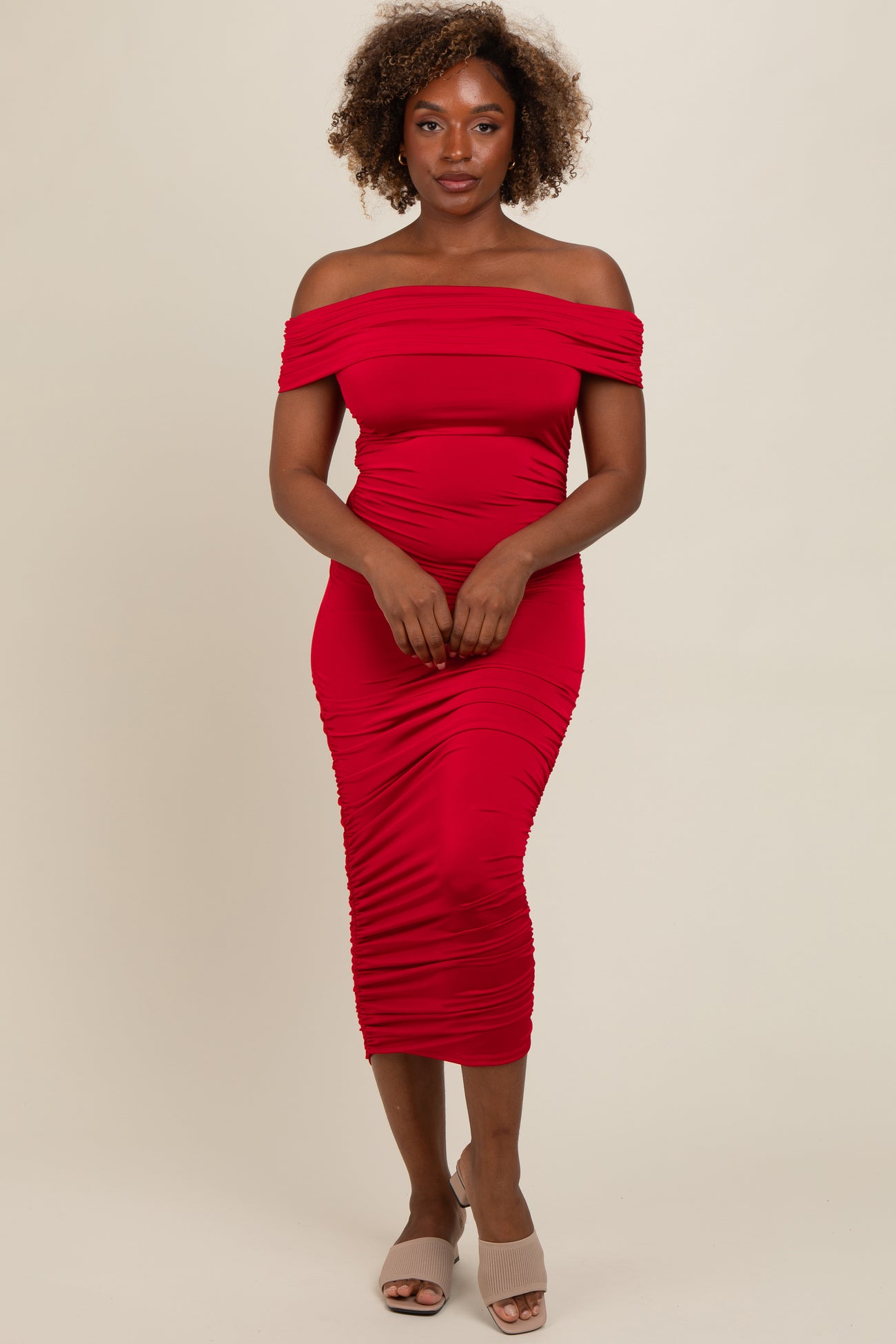 woman wearing a fitted red off-the-shoulder midi dress with ruching details and beige slide-on sandals