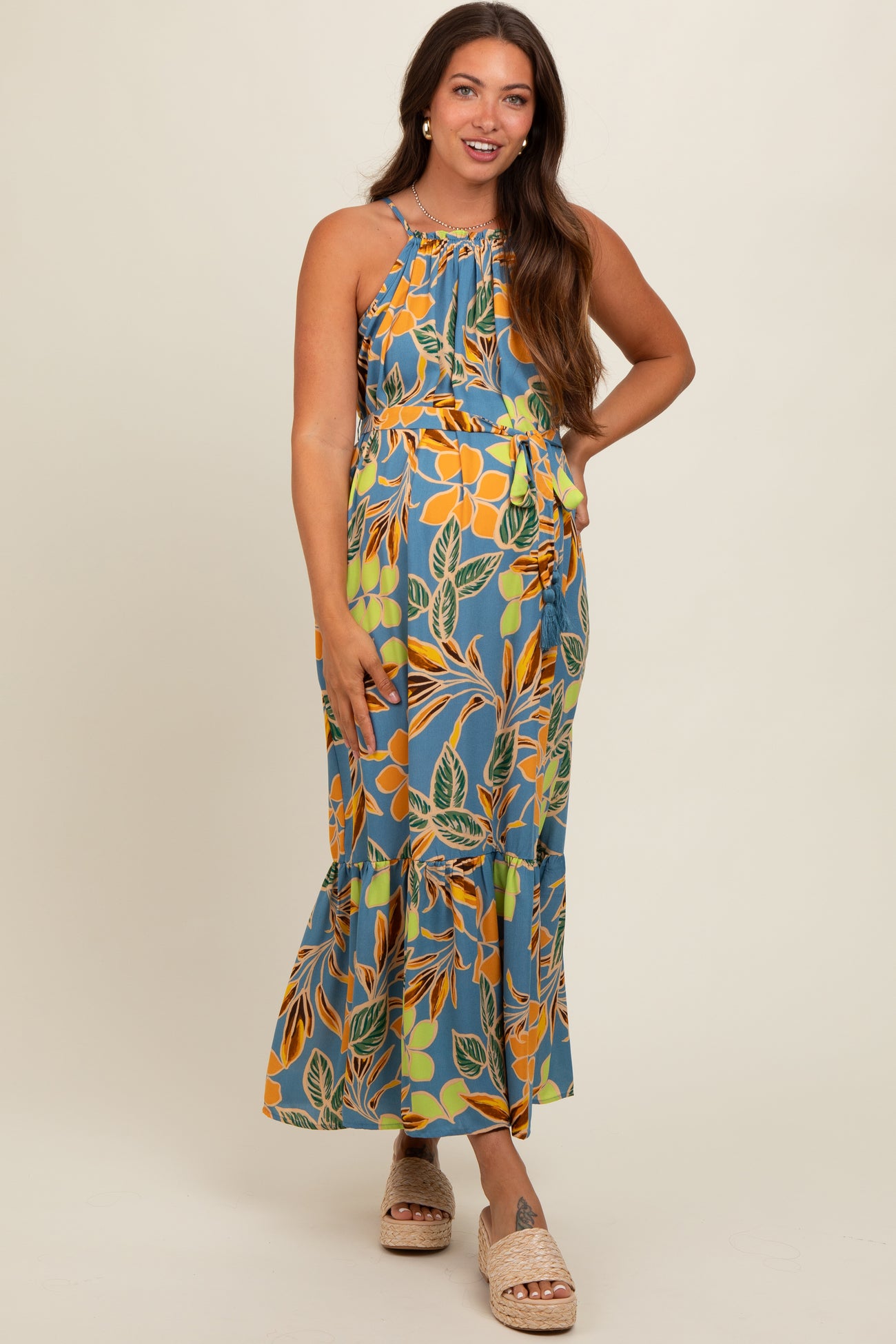 woman wearing a floral patterned maternity maxi dress with a halter neckline and ruffled hem, showcasing her baby bump
