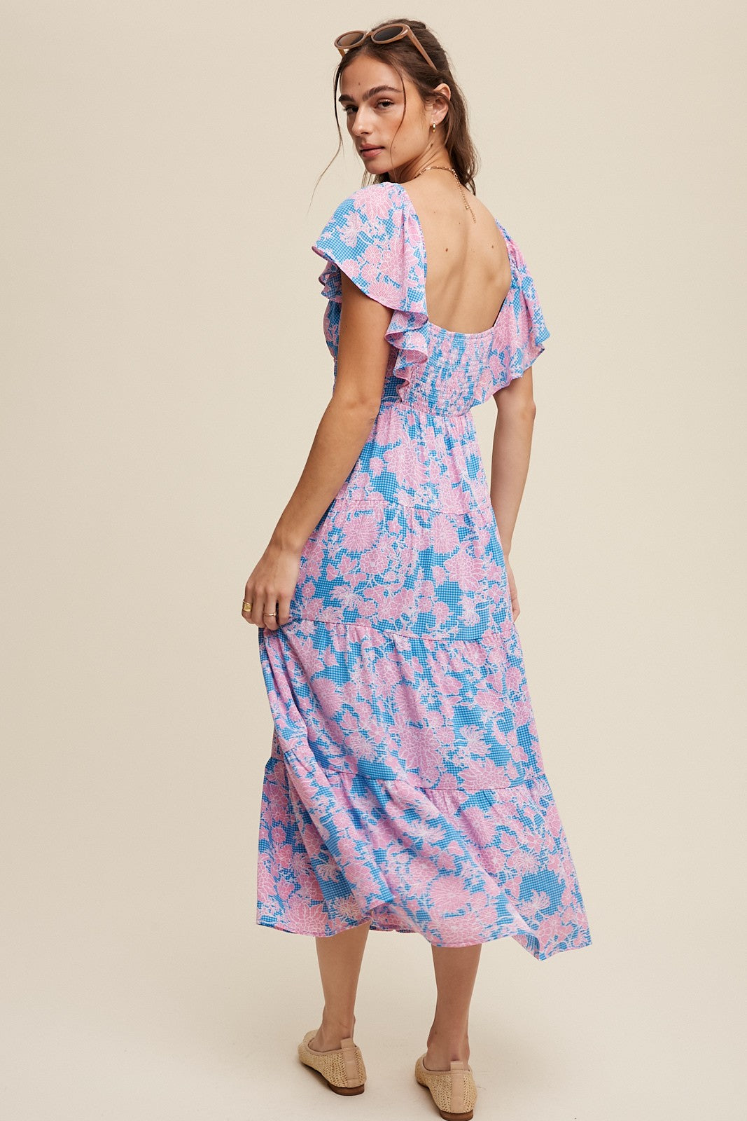 woman wearing a pink and blue floral maxi dress with ruffled sleeves and a low back, standing with her back to the camera