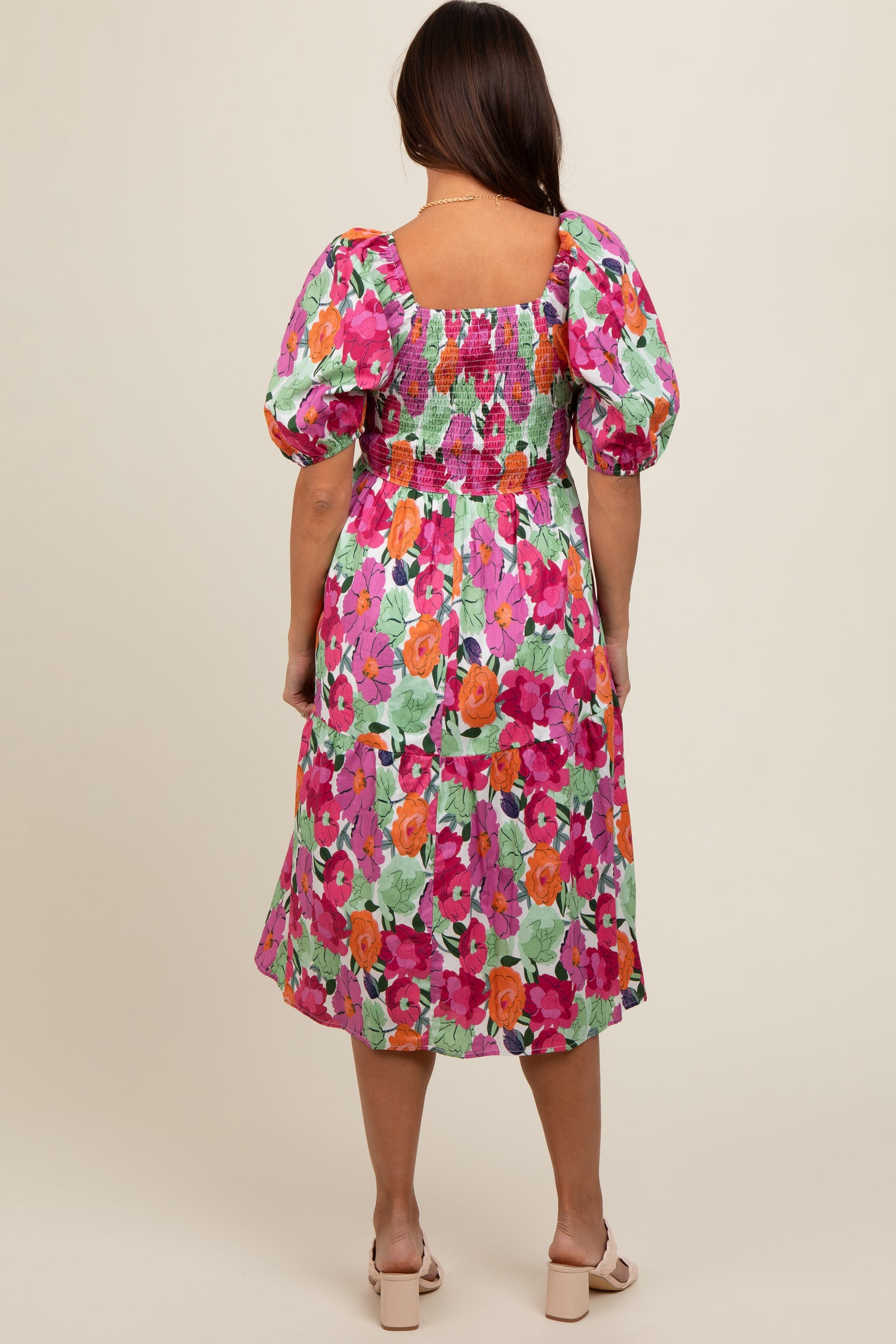 woman wearing a colorful floral maternity dress with puff sleeves and a smocked bodice, seen from the back