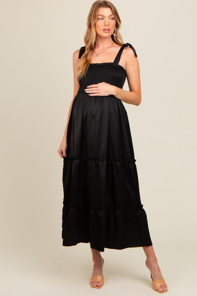 woman wearing a black maternity maxi dress with smocked bodice and ruffled bottom, holding her baby bump