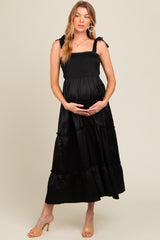 woman wearing a black maternity maxi dress with smocked bodice and tiered ruffle hem, holding her baby bump