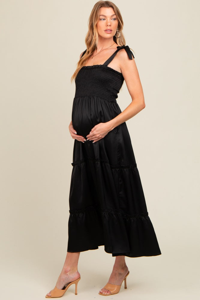 woman wearing a black maternity dress with smocked bodice and tiered skirt, holding her baby bump