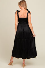woman wearing a black maxi maternity dress with smocked bodice and bow tie straps, showing her back and no baby bump visible