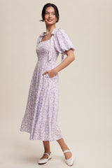 woman wearing a lavender floral midi dress with puff sleeves and pockets, smiling against a neutral background