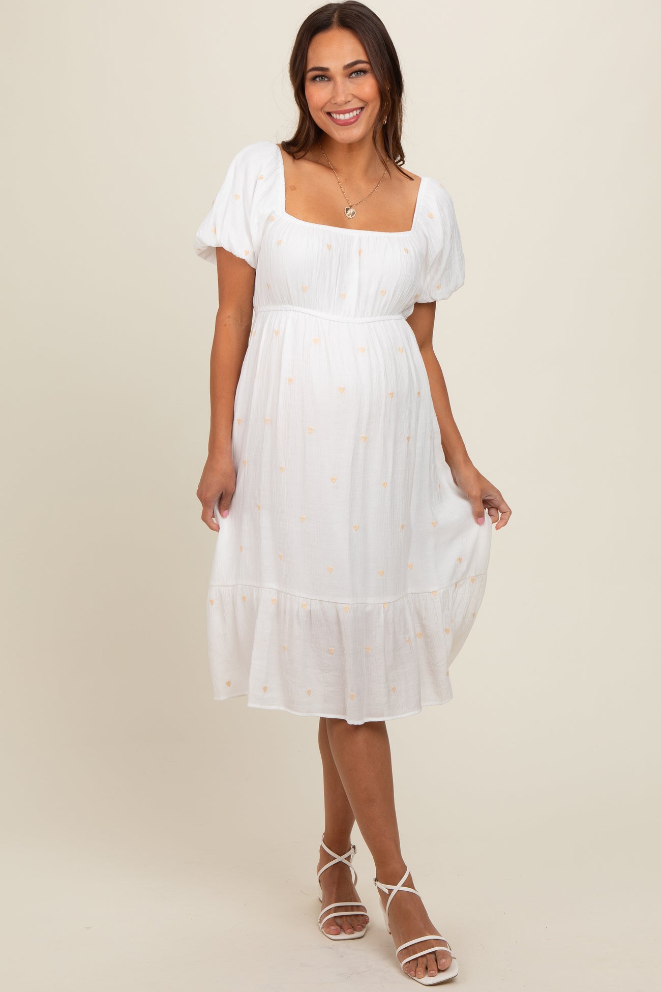 woman wearing a white maternity dress with puff sleeves and floral embroidery, showcasing her baby bump