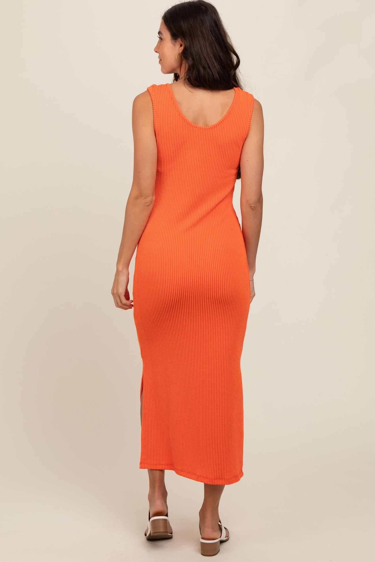 woman wearing an orange ribbed midi dress with side slits, viewed from the back