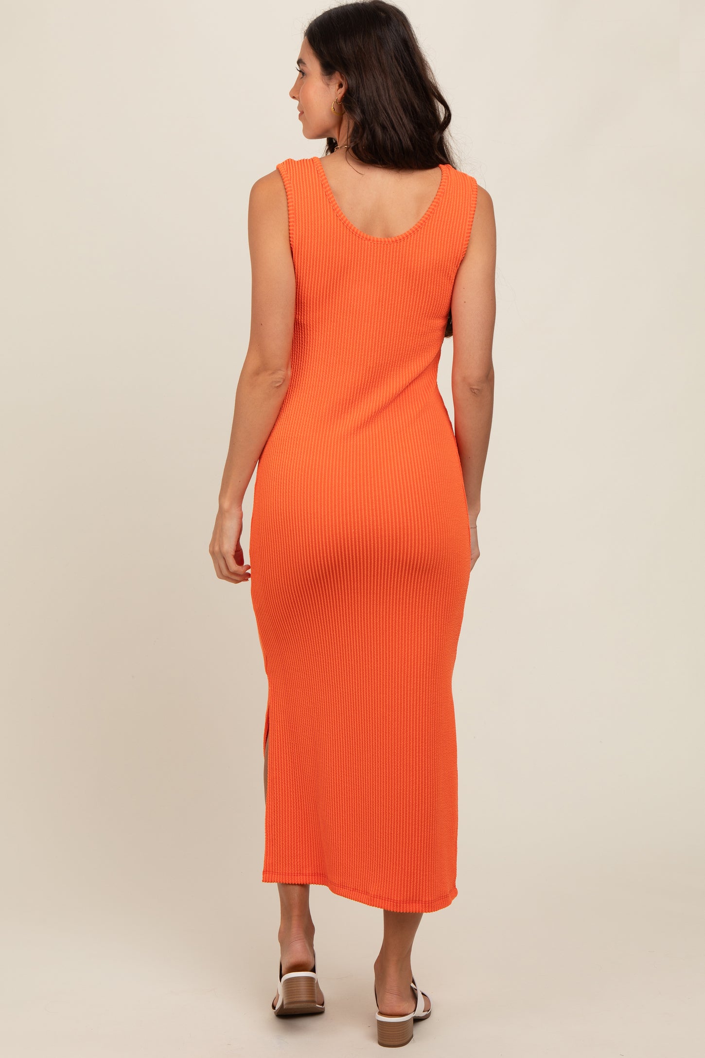 woman wearing an orange ribbed midi dress with side slits, viewed from the back