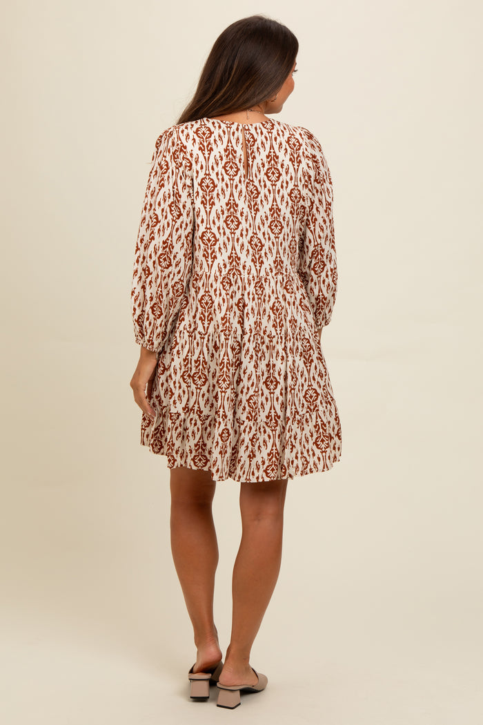 woman wearing a cream and rust-colored patterned maternity dress with long sleeves and a flared skirt, showing her back