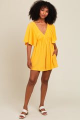 woman wearing a yellow short sleeve mini dress with a v-neck and flowy sleeves, standing with one hand in the pocket