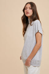 woman wearing a gray short sleeve mock neck sweater styled with light colored pants