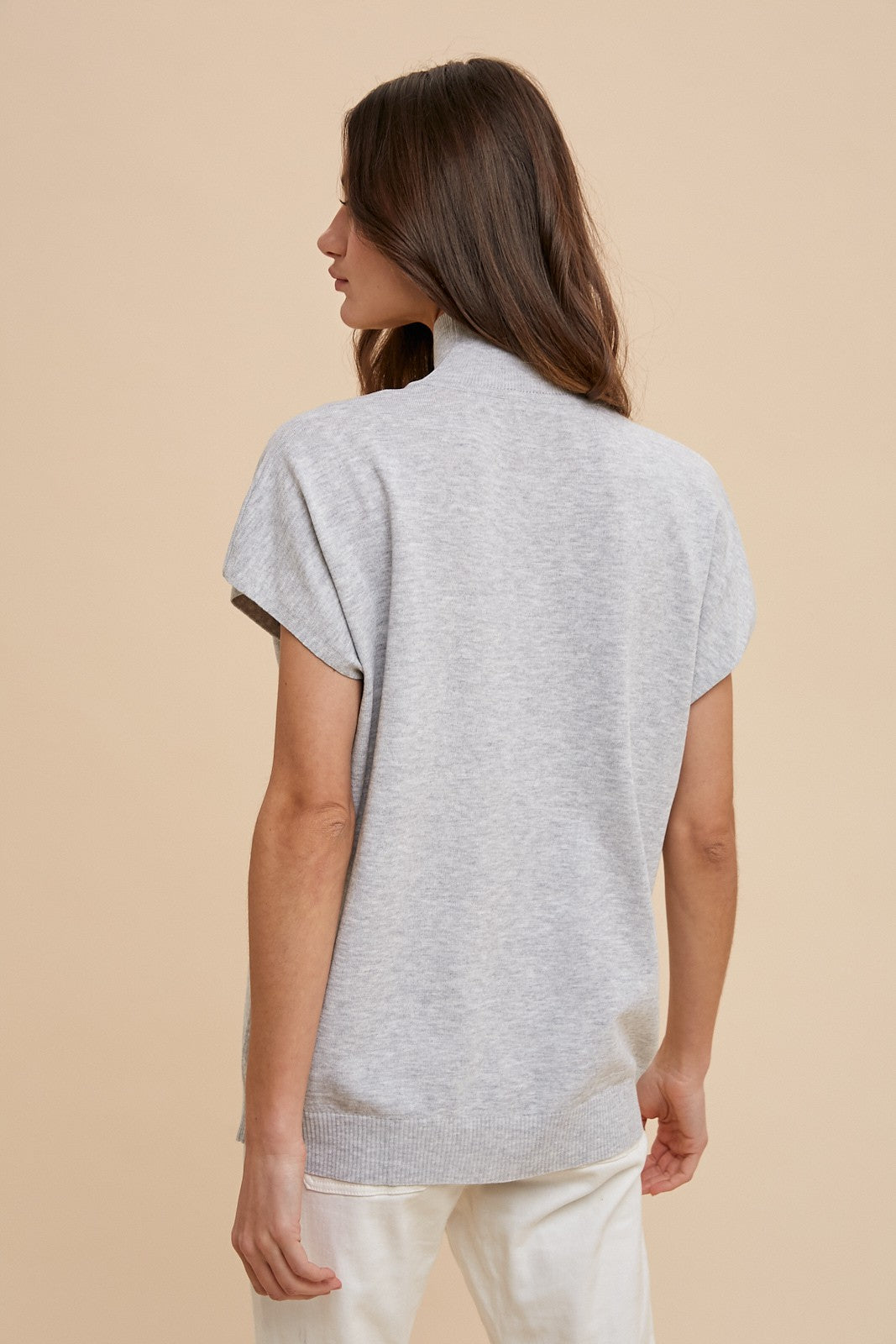 woman wearing a light gray short sleeve sweater with a mock neck and relaxed fit viewed from the back