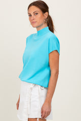woman wearing a bright turquoise short sleeve mock neck top and a white denim skirt