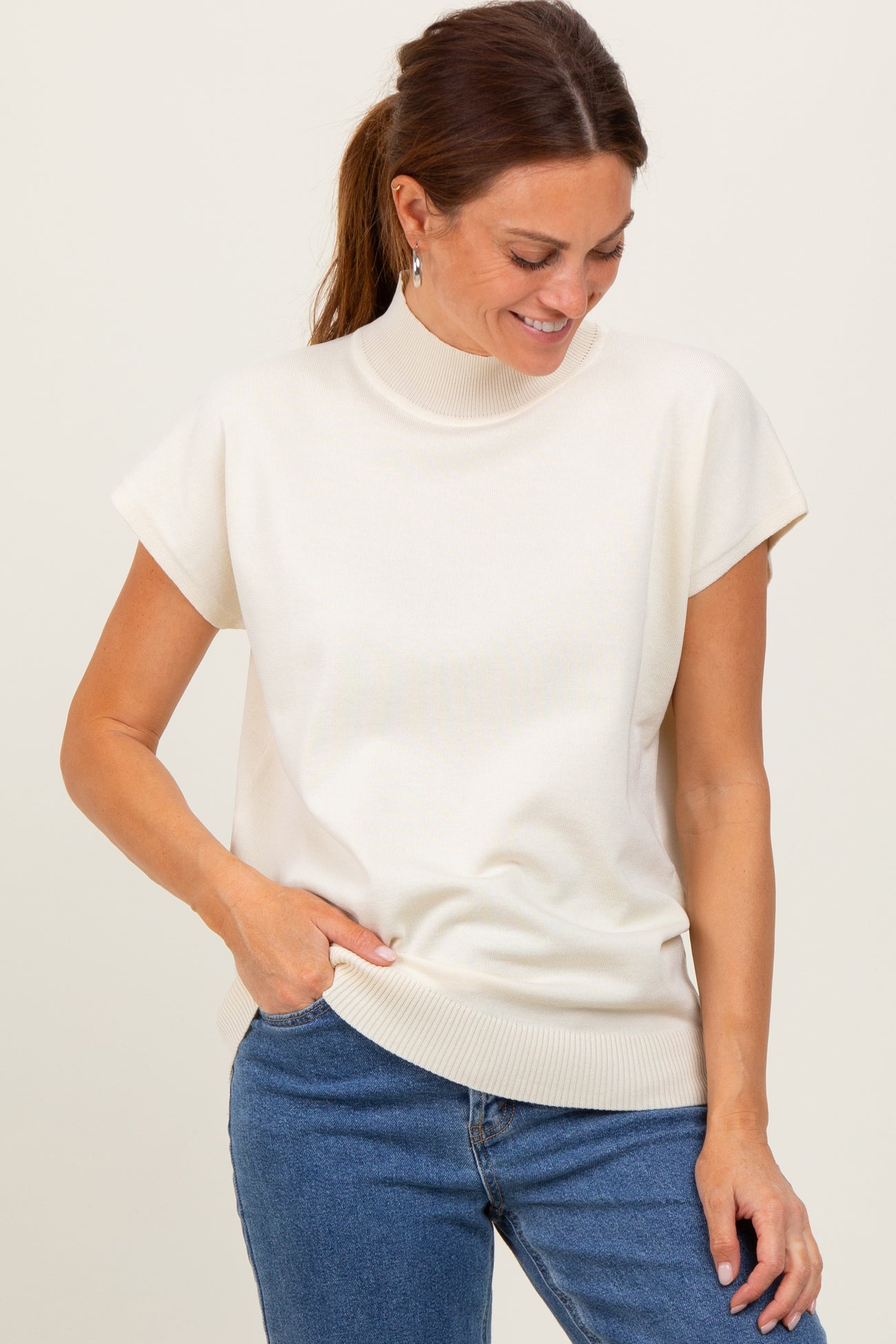 woman wearing a cream short sleeve mock neck sweater and blue jeans, smiling while looking down