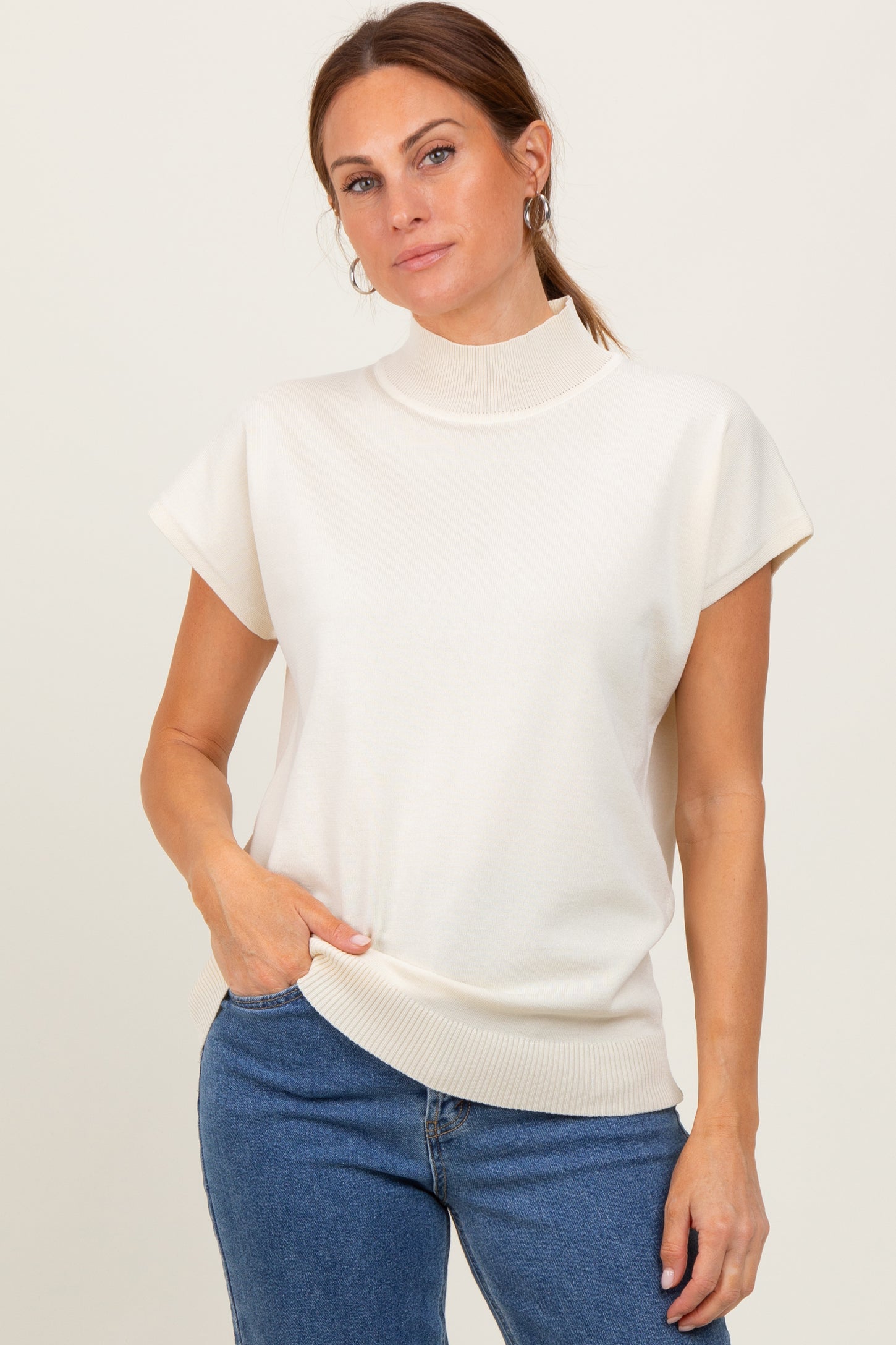 woman wearing a cream short sleeve turtleneck top with ribbed details and blue jeans