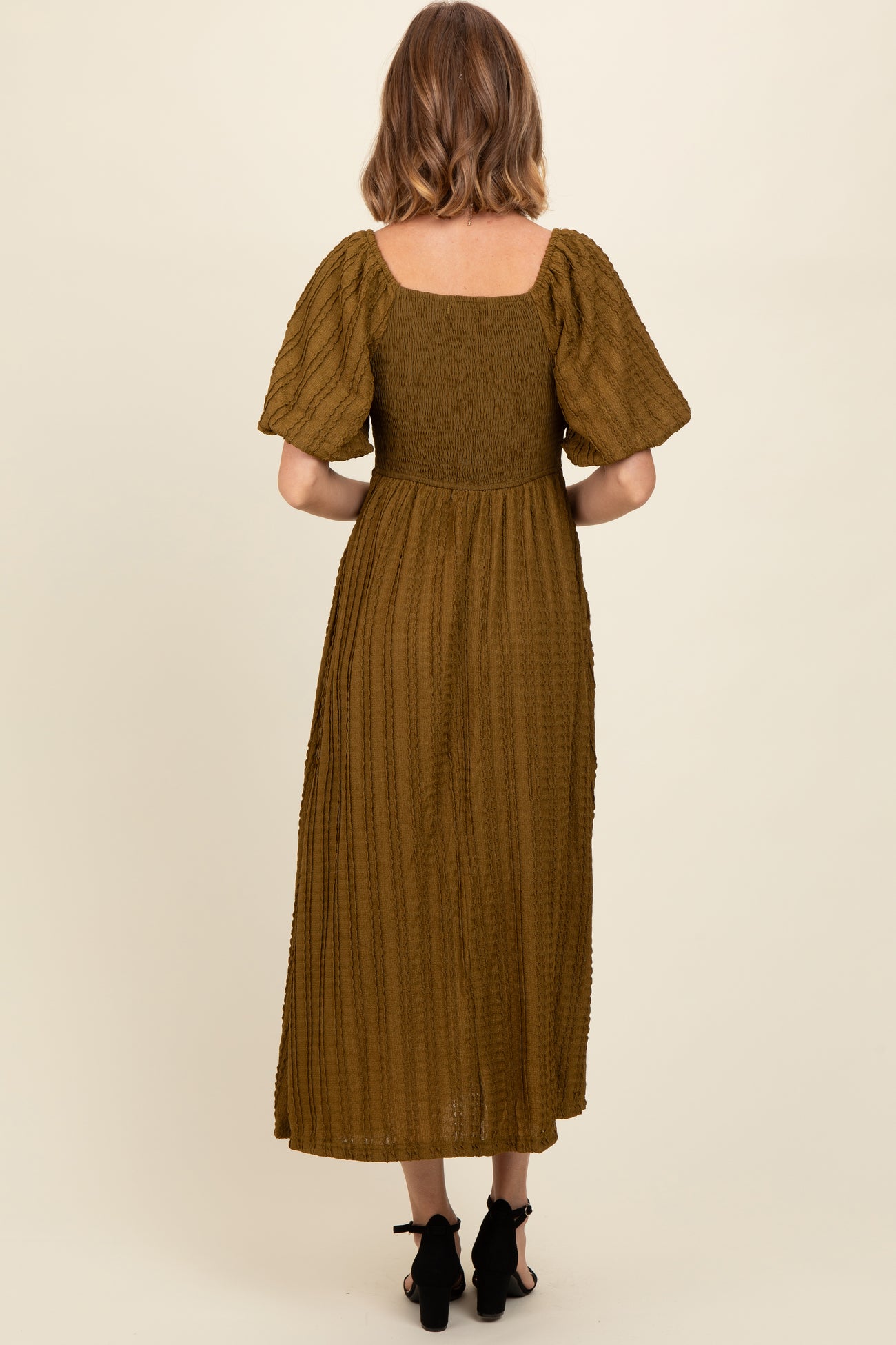 woman wearing a moss green smocked back midi dress with short puff sleeves and a flowing skirt