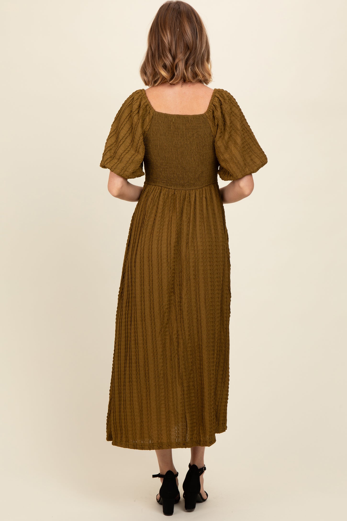 woman wearing a moss green smocked back midi dress with short puff sleeves and a flowing skirt