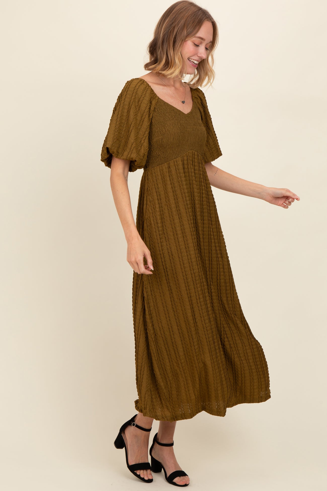 woman wearing a mustard brown midi dress with puffed sleeves and a fitted bodice, smiling while standing against a neutral background