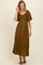 woman wearing an olive green maxi dress with puff sleeves and textured fabric, standing and smiling