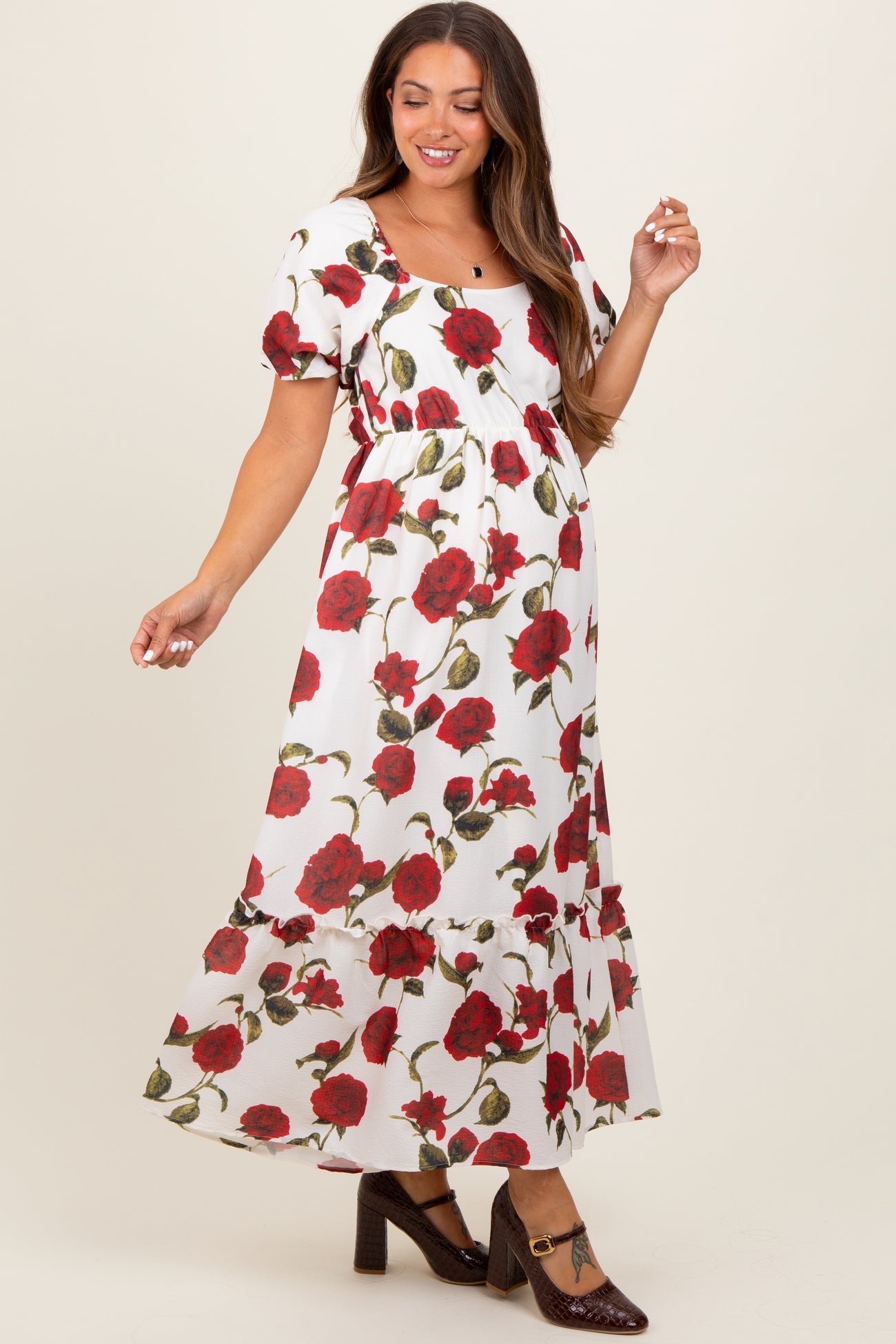 woman wearing a white floral maternity maxi dress with red roses and puff sleeves, showcasing her baby bump