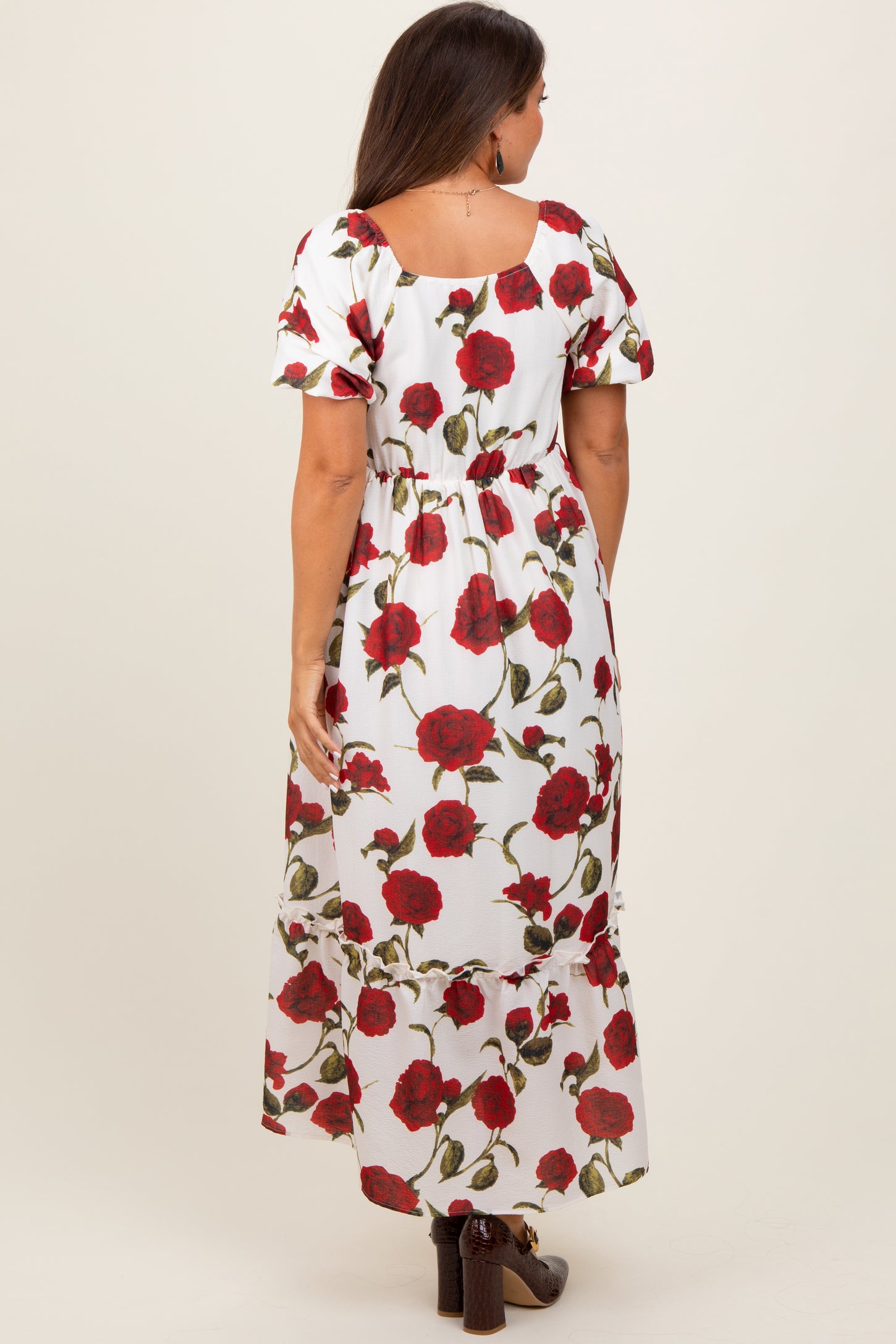 woman wearing a floral maternity maxi dress with red roses on a white background, showing a baby bump from the back
