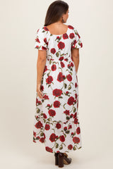 woman wearing a floral maternity maxi dress with red roses on a white background, showing a baby bump from the back
