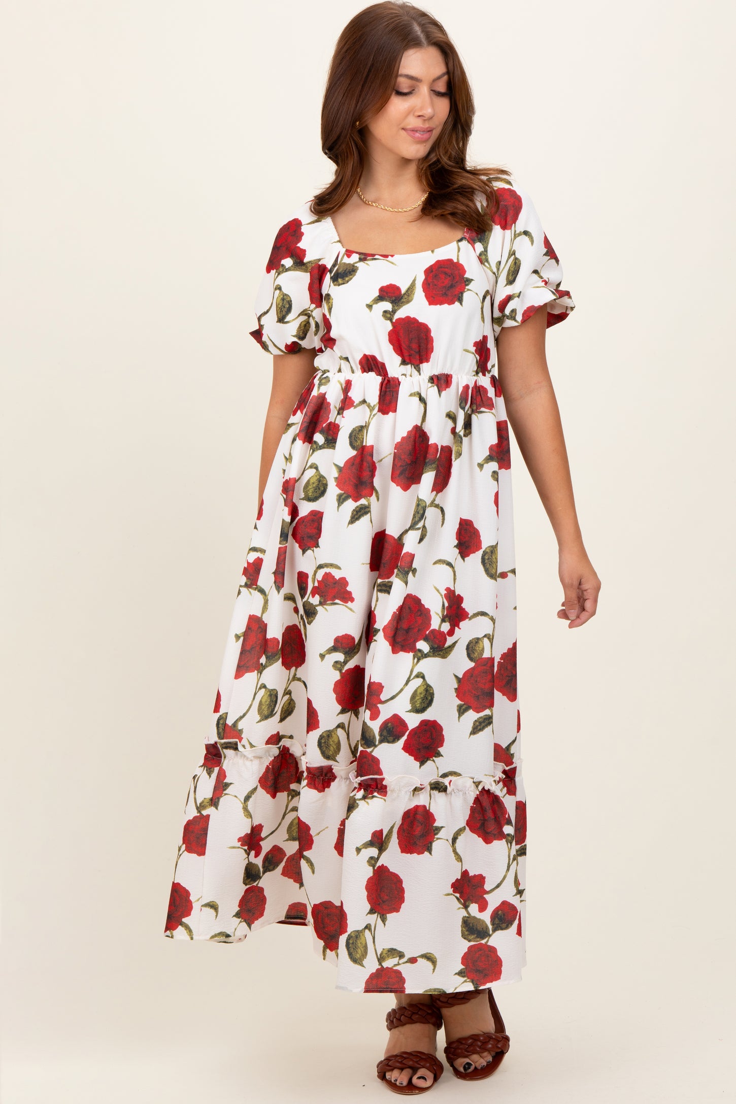 woman wearing a white floral maxi dress with red roses and puff sleeves, standing and looking down