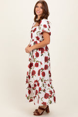 woman wearing a white floral maxi dress with red roses and puff sleeves, posed sideways against a neutral backdrop