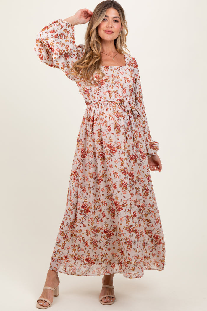 woman wearing a floral print maternity maxi dress with balloon sleeves and a cinched waist, smiling and posing
