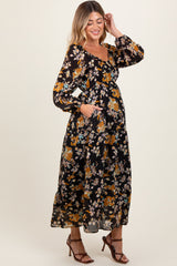 woman wearing a black floral maternity maxi dress with long sleeves and pockets, showing her baby bump