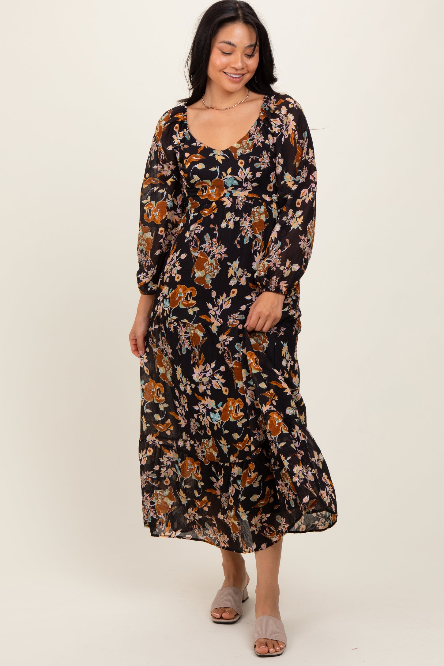 woman wearing a black floral maxi dress with long sleeves and a scoop neckline, smiling while standing
