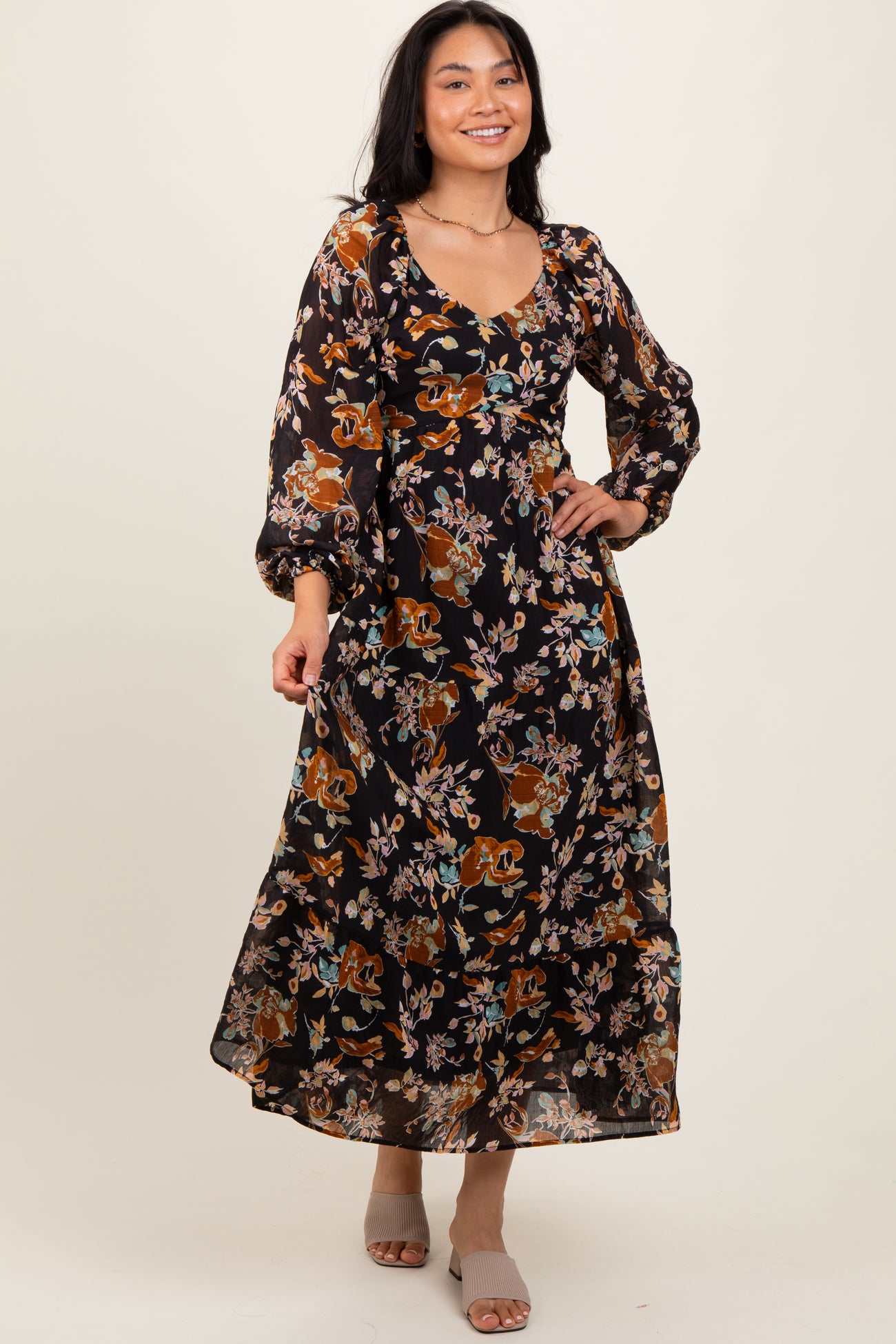 woman wearing a black floral maxi dress with long sleeves and a v-neckline, smiling in a studio setting