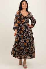 woman wearing a black floral maxi dress with long sleeves and a v-neckline, smiling in a studio setting