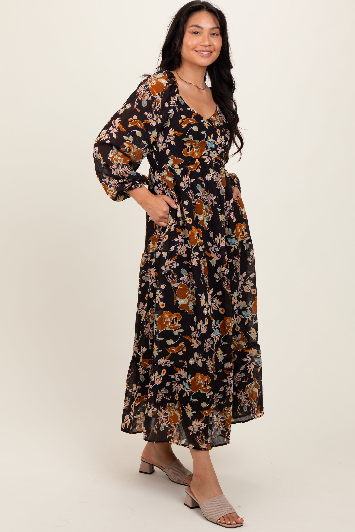 woman wearing a black floral maxi dress with long sleeves and pockets, standing in profile