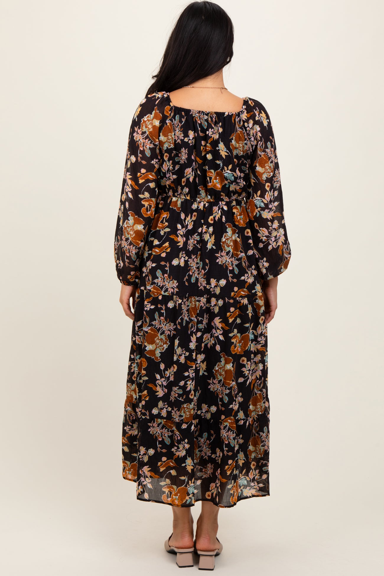 woman wearing a black floral maxi dress with long sleeves and a tiered back detail, seen from the back